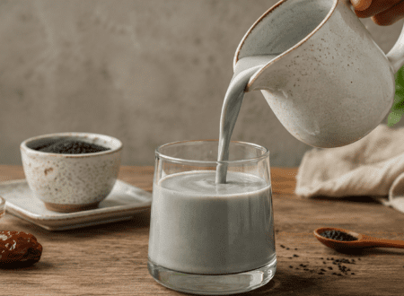 Homemade black sesame milk served in a glass with black sesame seeds scattered around on a wooden surface.
