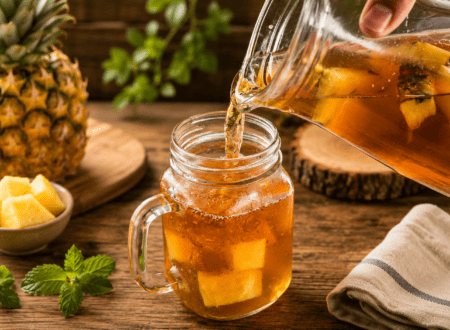 Glass of iced pineapple tea garnished with pineapple wedges, lemon slices, mint leaves, and ice cubes.