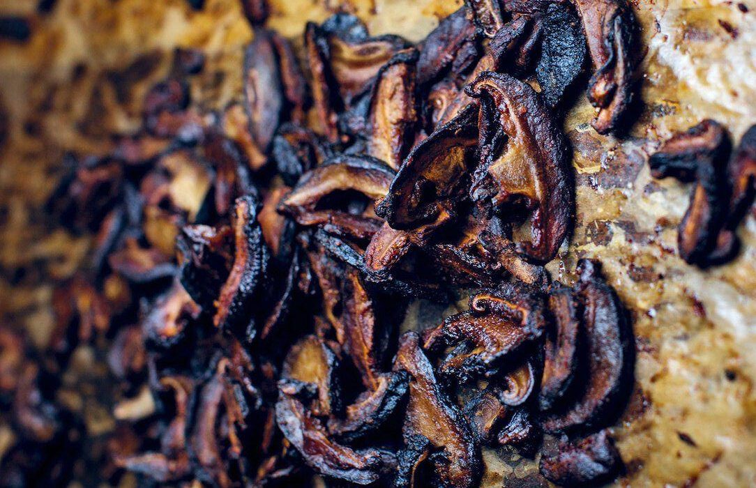 Crispy shiitake bacon strips on a plate with smoky seasoning and fresh herbs.