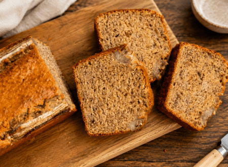 Slices of gluten-free dairy-free banana bread on a wooden board with fresh bananas nearby.