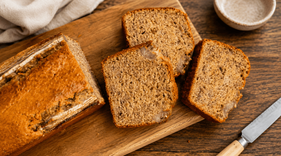 Slices of gluten-free dairy-free banana bread on a wooden board with fresh bananas nearby.