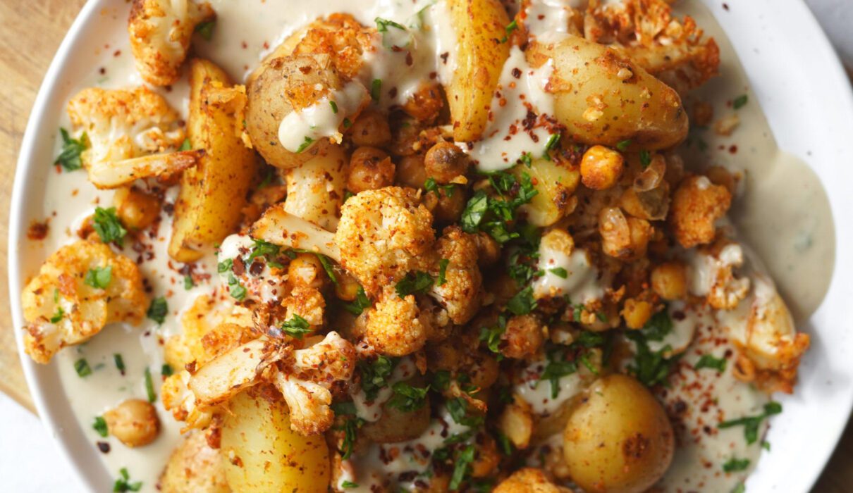 Roasted cauliflower, chickpeas, and potatoes served in a bowl with creamy tahini sauce and fresh herbs.