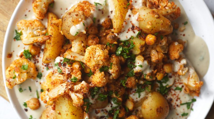 Roasted cauliflower, chickpeas, and potatoes served in a bowl with creamy tahini sauce and fresh herbs.