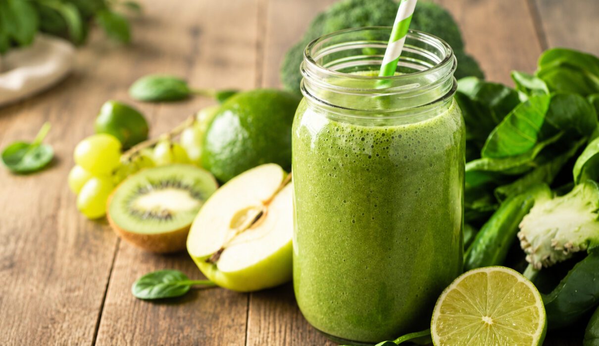 Healthy spirulina smoothie in a glass with vibrant green color and fresh fruit nearby.