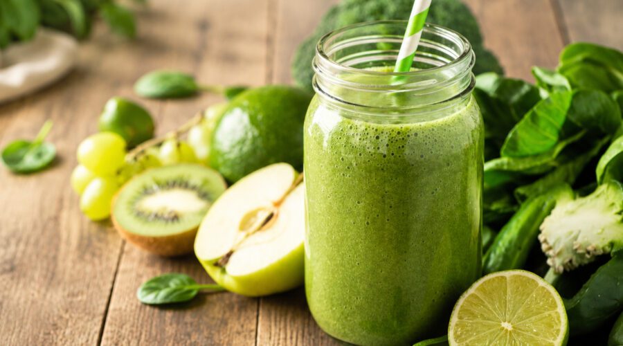 Healthy spirulina smoothie in a glass with vibrant green color and fresh fruit nearby.
