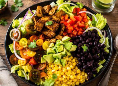 Colorful taco salad topped with lettuce, beans, tomatoes, avocado, corn, and crunchy tortilla strips.
