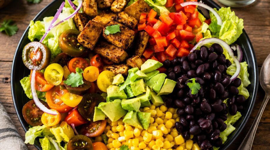 Colorful taco salad topped with lettuce, beans, tomatoes, avocado, corn, and crunchy tortilla strips.