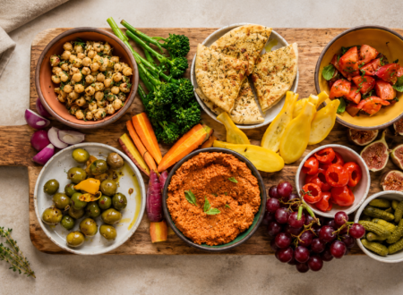 Colorful vegan charcuterie board with plant-based cheeses, fruits, crackers, nuts, olives, and dips.