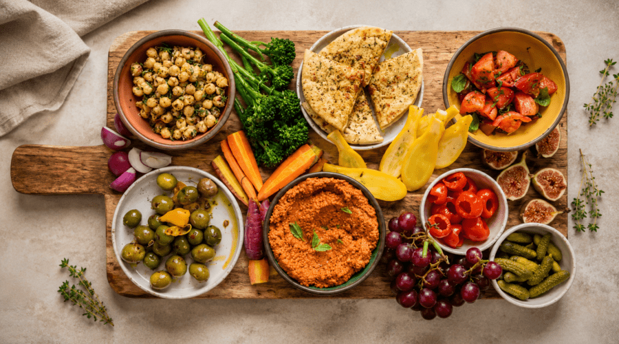 Colorful vegan charcuterie board with plant-based cheeses, fruits, crackers, nuts, olives, and dips.