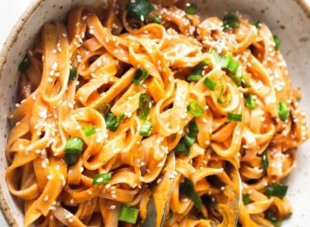 Bowl of creamy Thai red curry noodles with vegetables, tofu, fresh cilantro, and lime wedges.