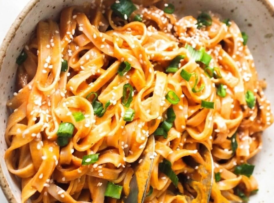 Bowl of creamy Thai red curry noodles with vegetables, tofu, fresh cilantro, and lime wedges.